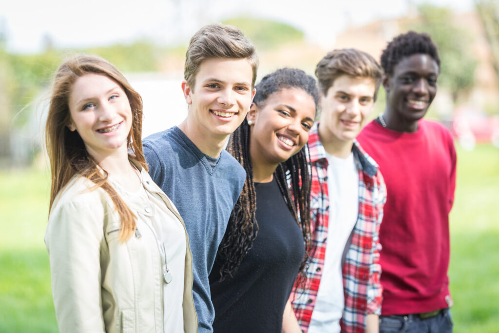 Portrait image of five multiethnic teenagers smiling outdoors.