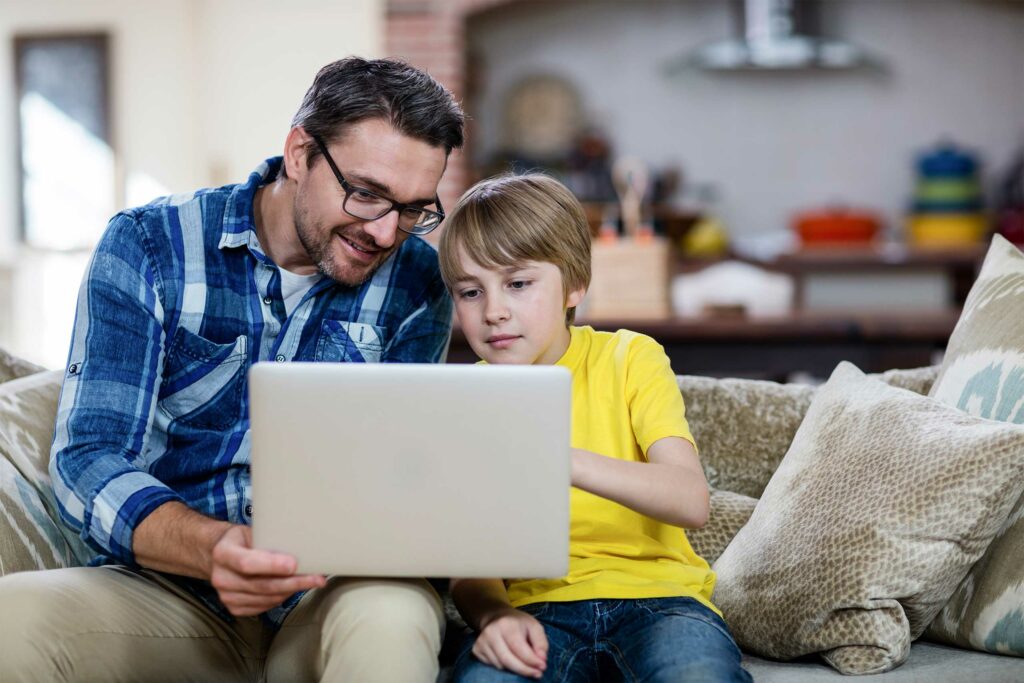 Father and son using laptop in living room at home.